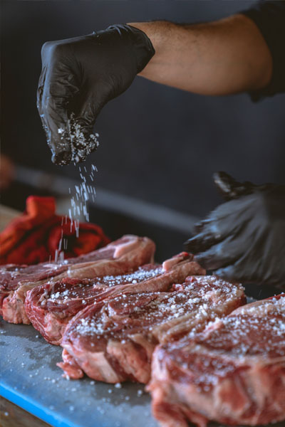 manos salando carne cruda